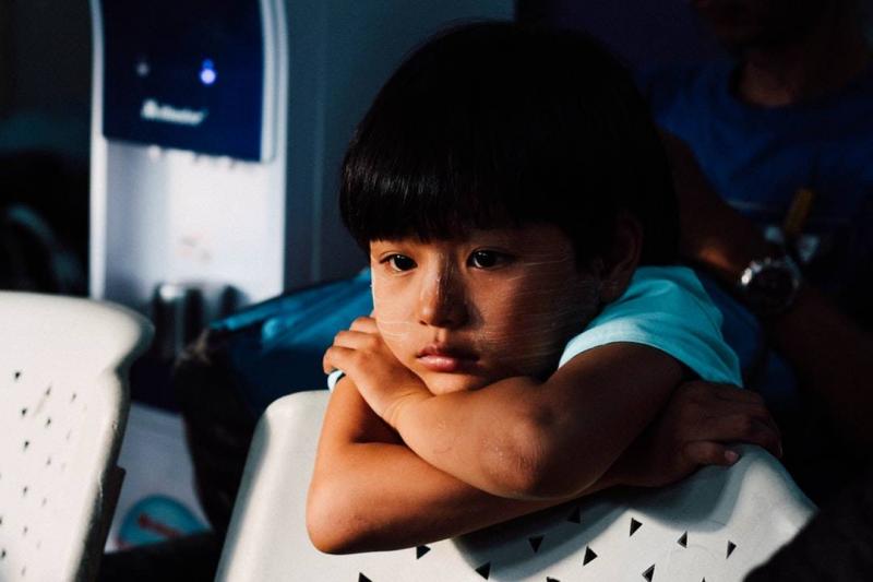 Young boy sad, leaning on his folded arms over a chair.