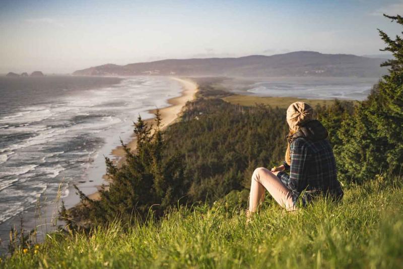 Woman sitting on a hill overlooking a tree-filled ocean shoreline.