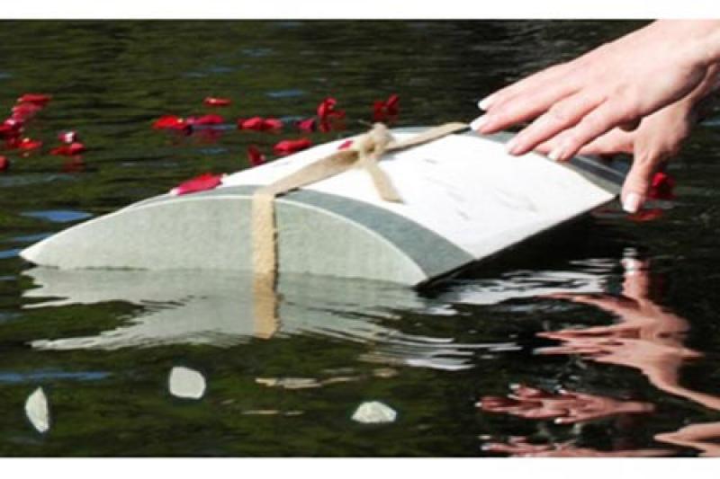 Biodegradable burial urn being released on the water with rose petals.