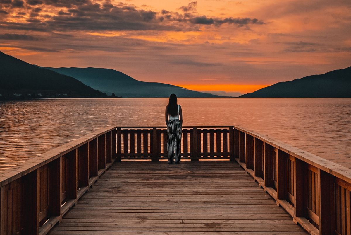Woman standing at the end of a dock overlooking the sunset.