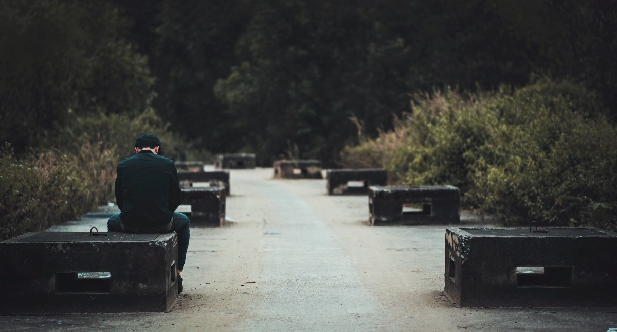 Man with his head down in sadness sitting on a bench.