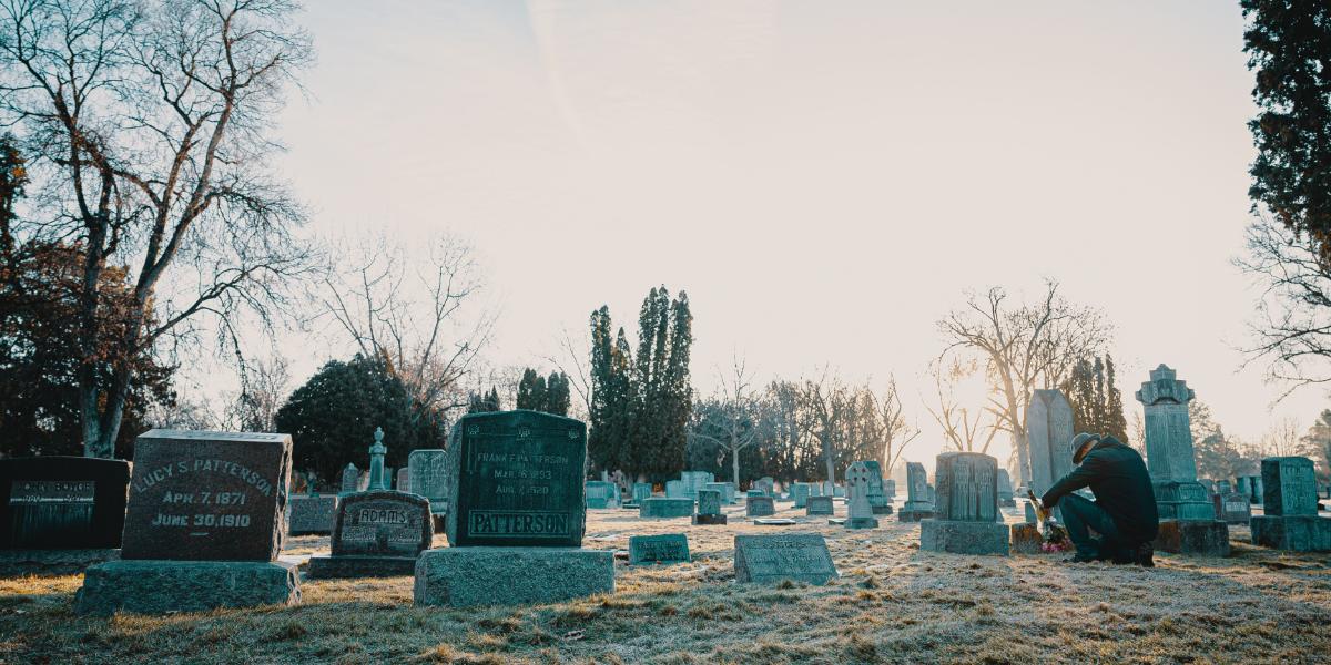 Man mourning next to headstones in cemetery at dawn.