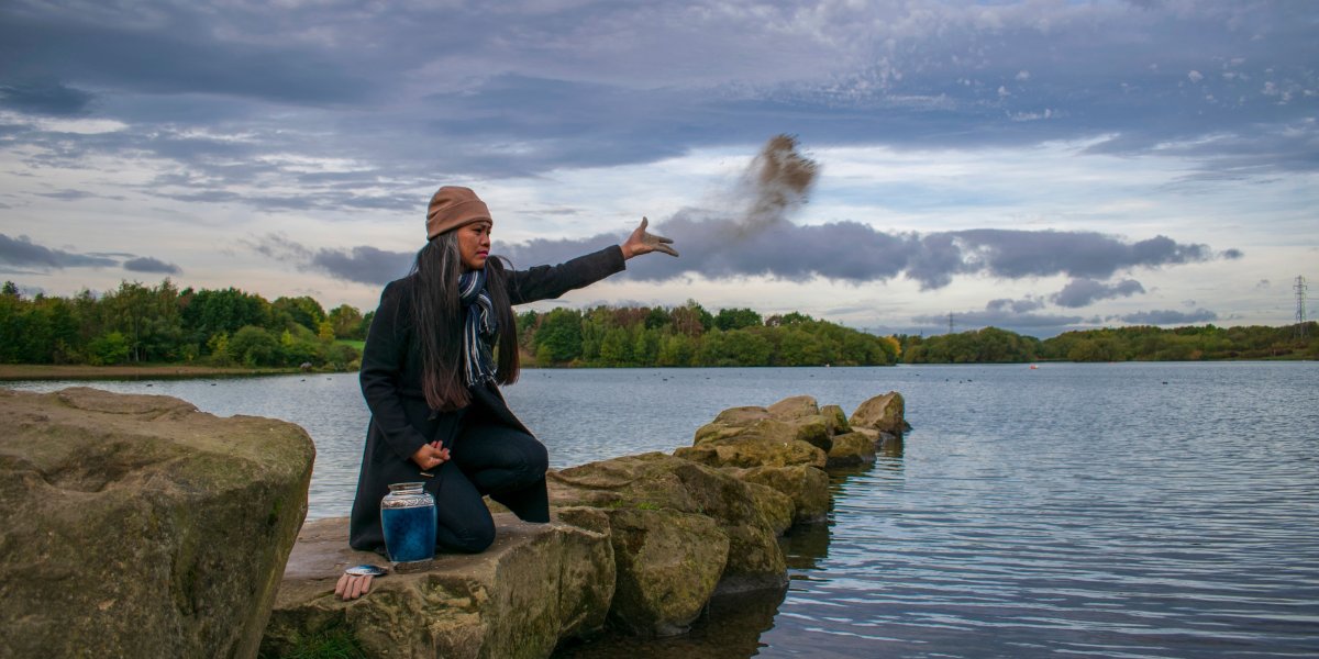 Woman scattering ashes on the edge of a lake at dusk.