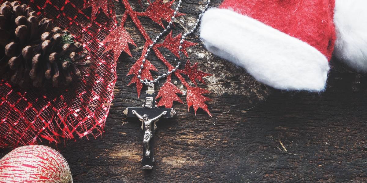 Jesus cross necklace on a wood log amongst Christmas decorations.