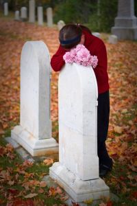 Woman holding pink flowers bowing head and crying on a headstone.
