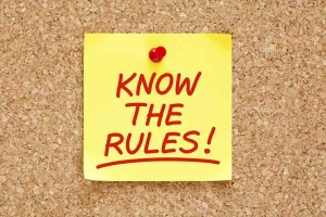 Yellow sticky note saying "Know The Rules!" pinned to cork board.
