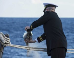 Man in military uniform scattering ashes into the ocean.