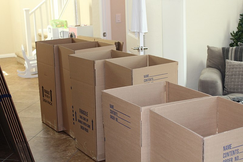 Moving boxes lined up by the door inside of a house.