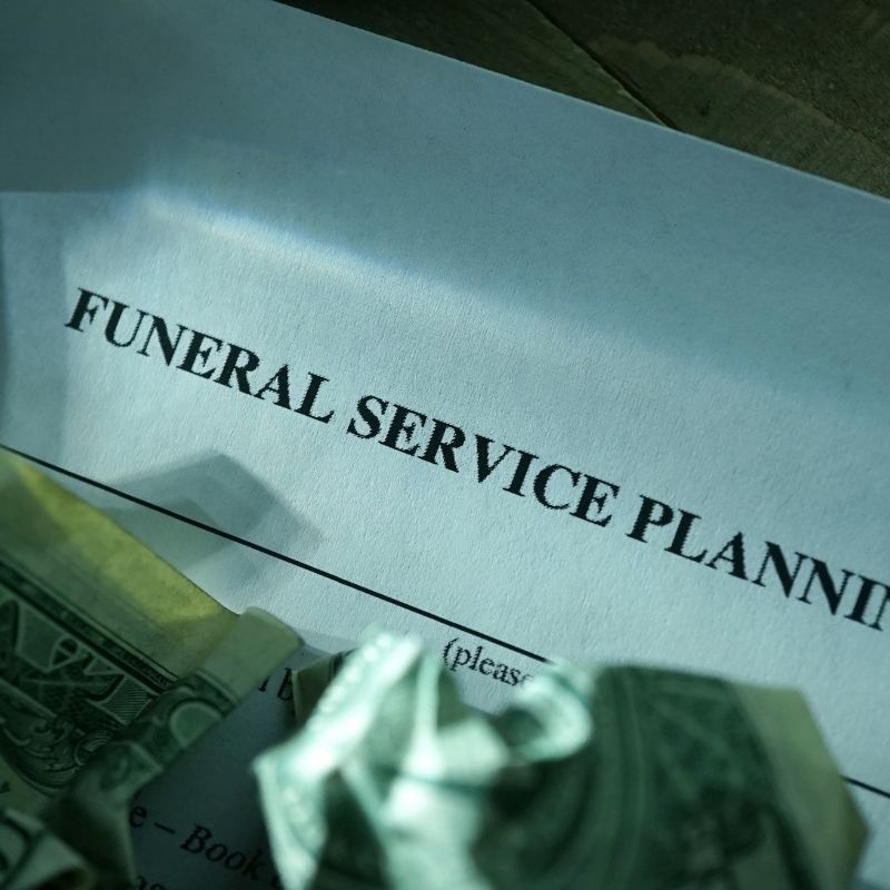 Crumpled dollar bills over paper document about funeral service planning.