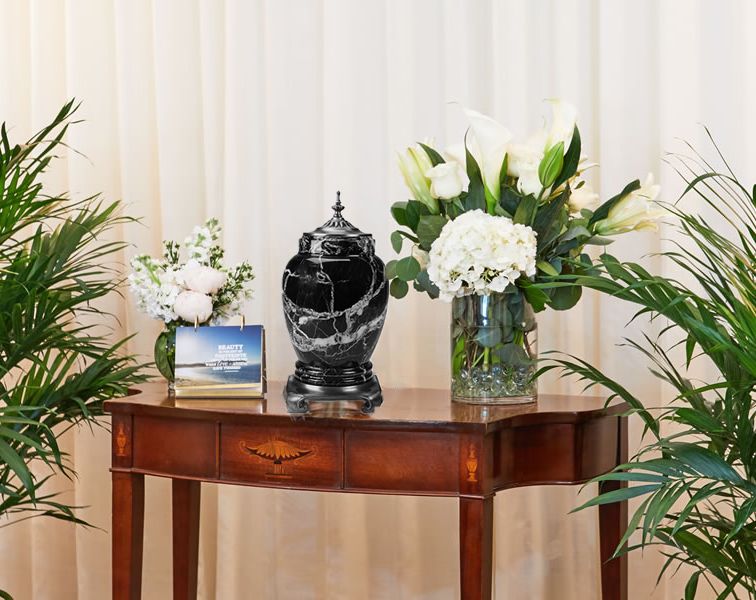 Cremation urn and flowers sitting on a medium brown table at a funeral.