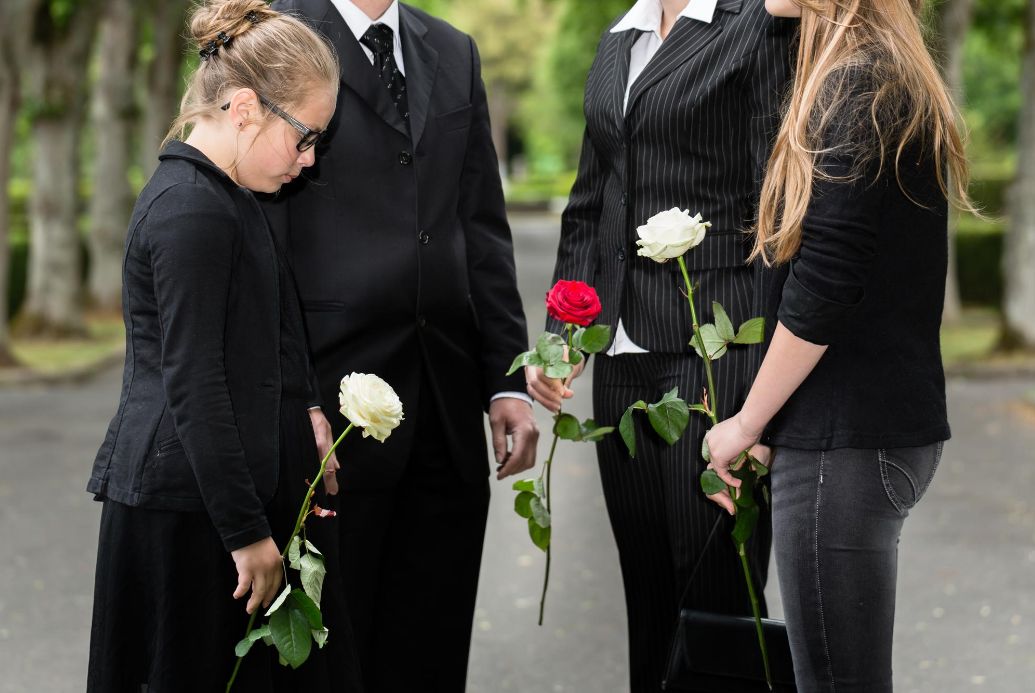 Group of 4 holding flowers mourning in black funeral attiire.