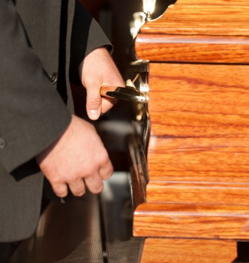 Close up of man in suit carrying a light brown casket.