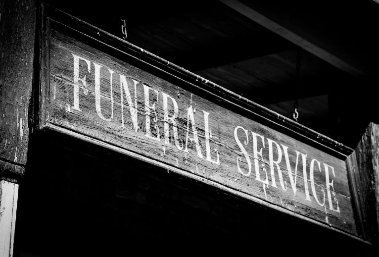 Rustic wooden sign with funeral service written in white.
