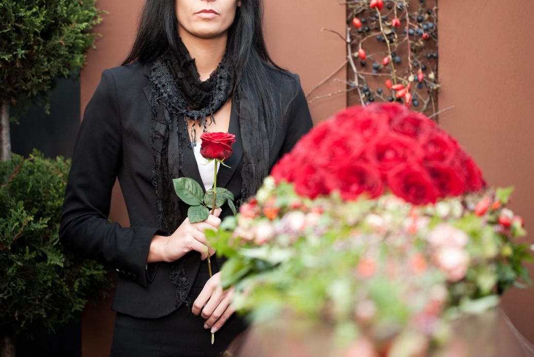 Woman with black hair holding a single rose mourning at a funeral.