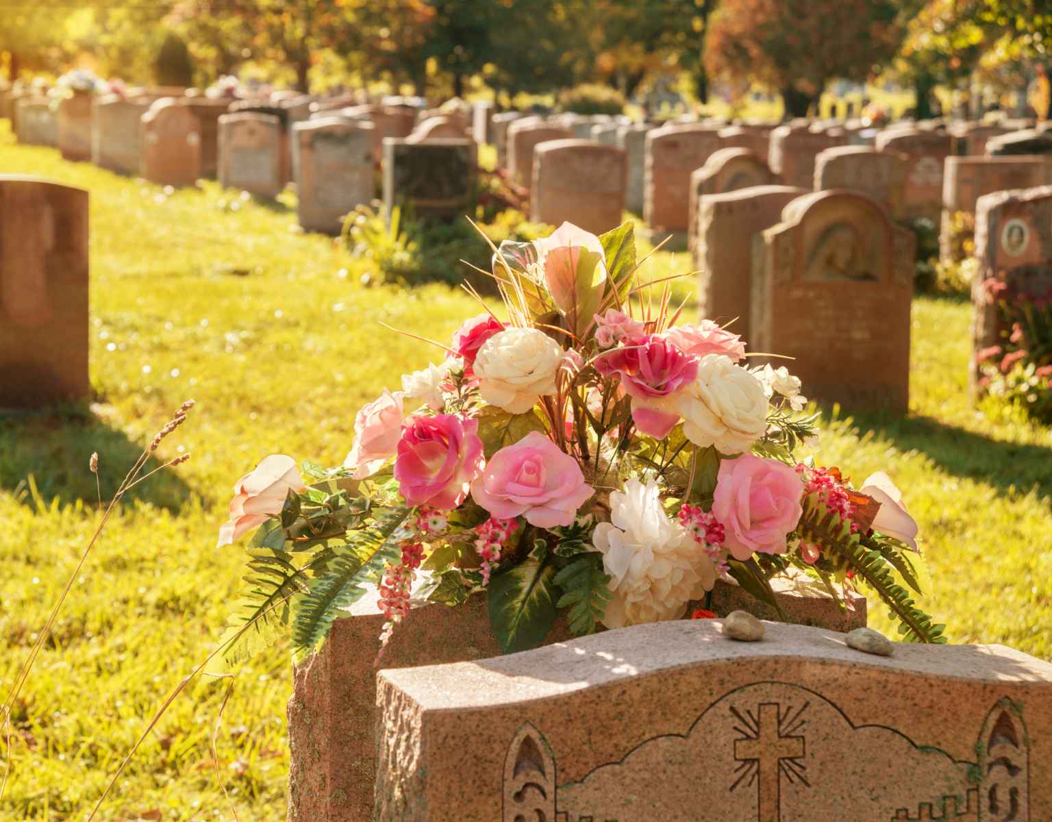 Headstone in cemetery with pink flower arrangement.