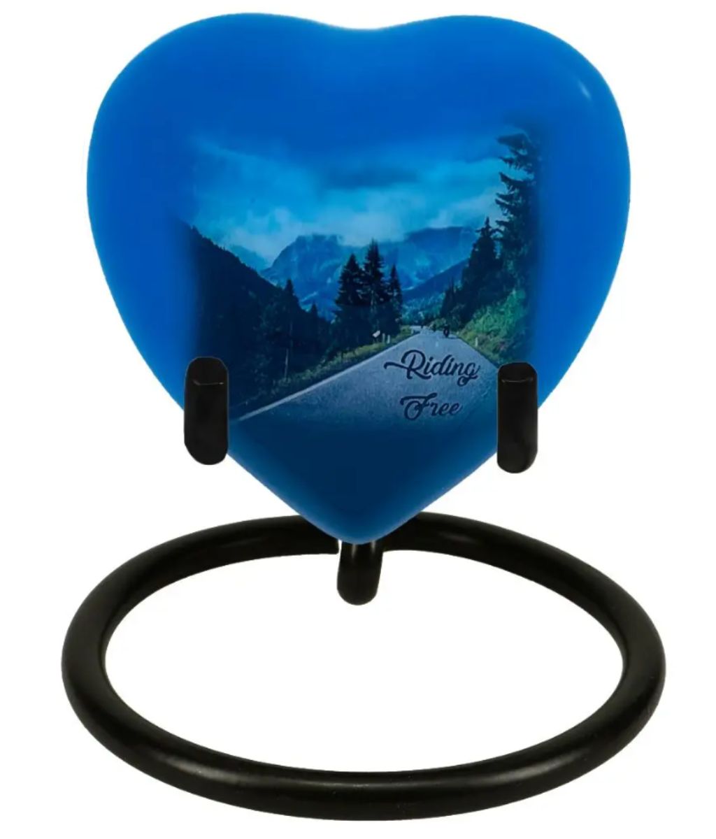 The Riding Free Heart Keepsake Urn - Stand Option shows several bikers riding through a mountain paradise. Perfect for dresser or night table, with a heart stand is an option.