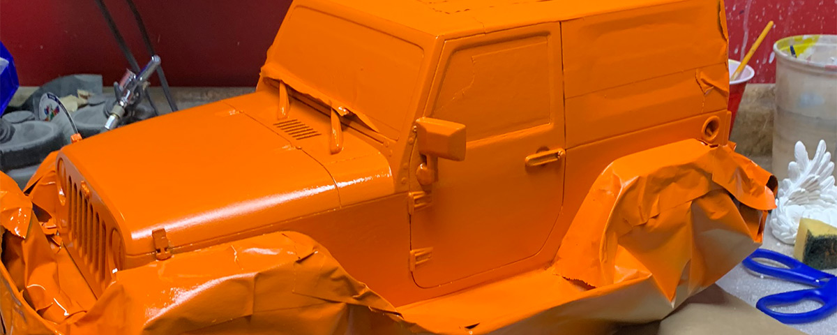 The 3D-printed Jeep is covered in painter's tape and painted a bright orange.