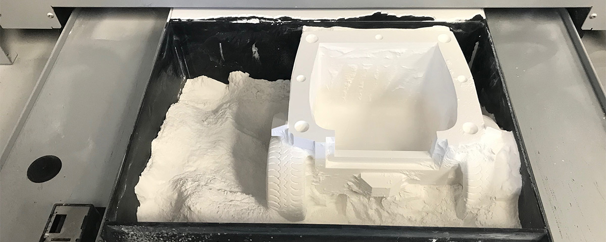 Half of the Jeep model is inside the powder bin of a 3D-printer.
