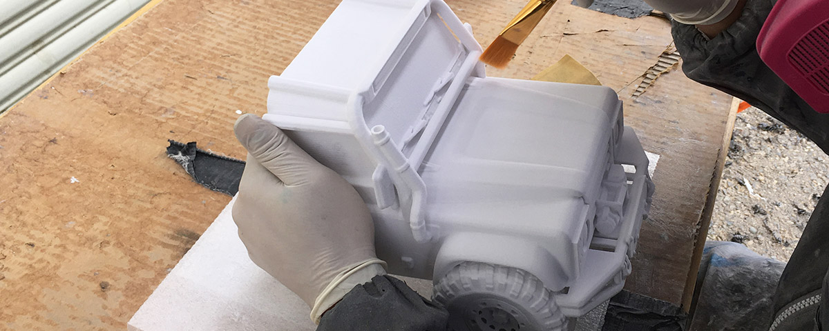 One half of the 3D-printed Land Rover is being brushed off with a paintbrush after leaving the 3D printer.