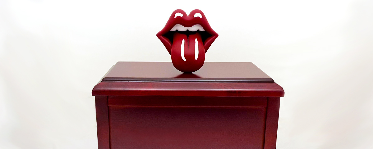 The 3D-printed tongue and lips on top of a wooden urn.