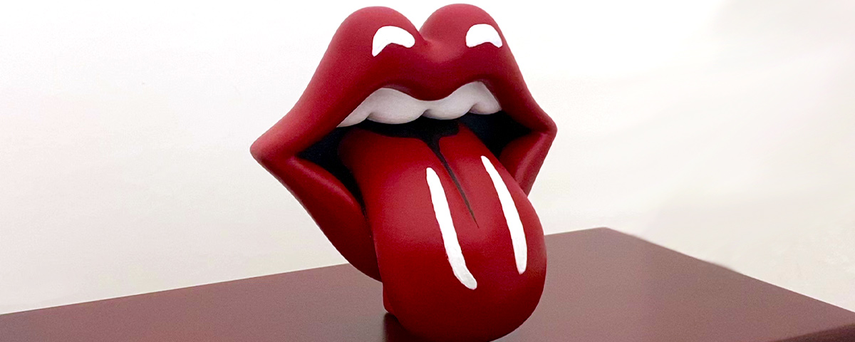 A close-up of the 3D-printed tongue and lips design on top of a wooden urn.