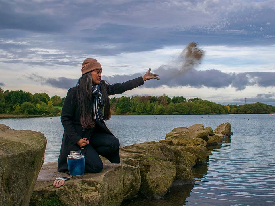 Woman casting cremated remains along the side of a lake.