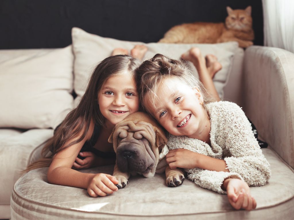 Two girls cuddled up next to a pug on the couch.