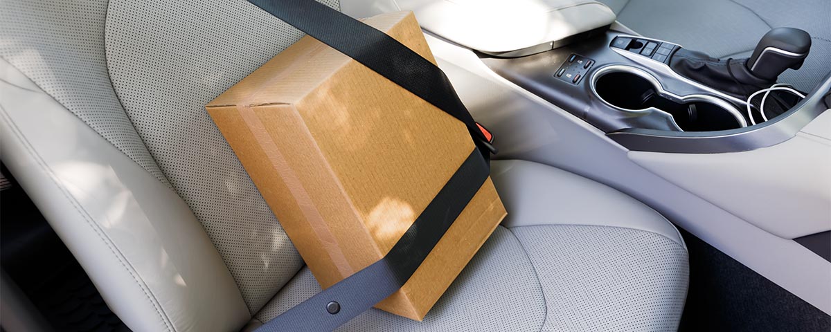 A sealed cardboard box is buckled into the passenger seat of a car.